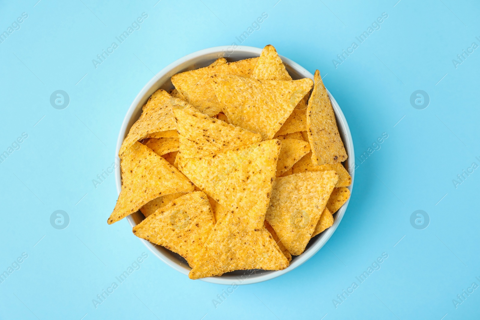 Photo of Bowl with tasty Mexican nachos chips on light blue background, top view