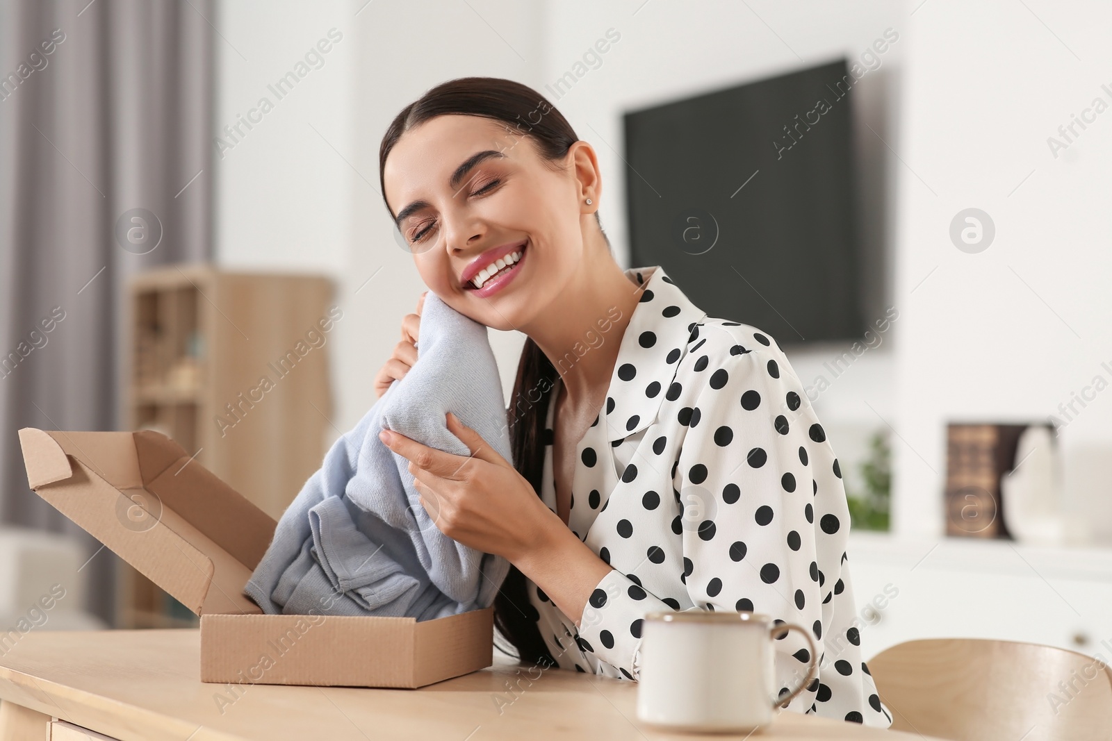 Photo of Happy young woman with parcel at table indoors. Internet shopping