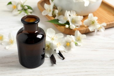 Jasmine essential oil and fresh flowers on white wooden table, space for text