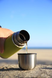 Photo of Woman pouring hot drink from yellow thermos into cap on stone surface outdoors, closeup