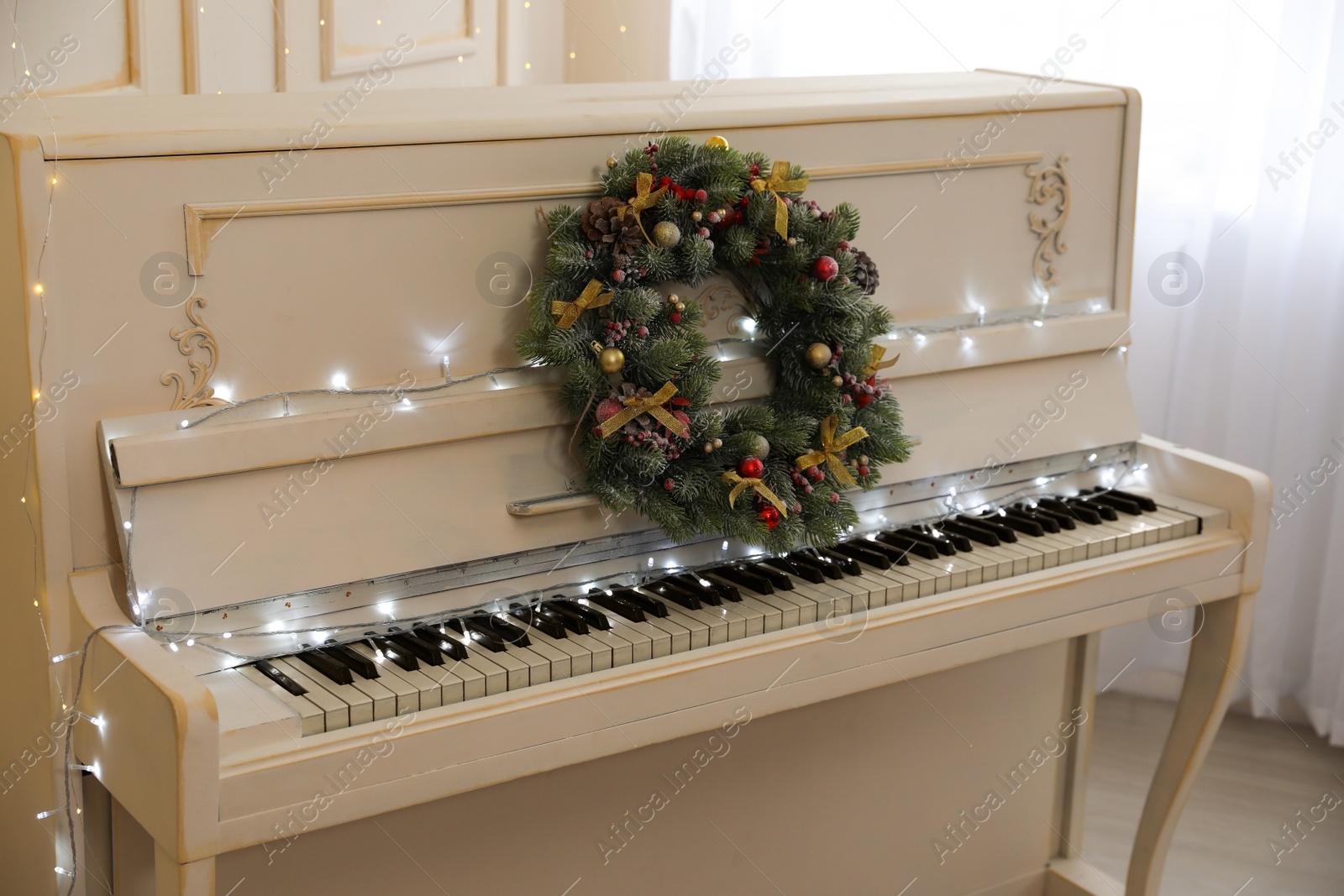 Photo of White piano with fairy lights and decorative wreath indoors. Christmas music