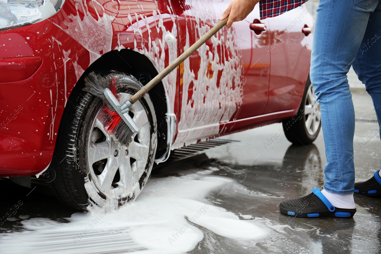 Photo of Young man cleaning vehicle with brush at self-service car wash