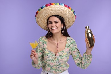 Photo of Young woman in Mexican sombrero hat with cocktail and shaker on violet background