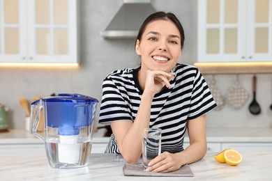 Photo of Woman with glass of water and filter jug in kitchen