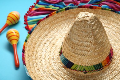 Photo of Mexican sombrero hat, maracas and colorful poncho on light blue background