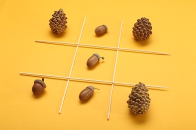 Photo of Tic tac toe game made with acorns and pine cones on yellow background