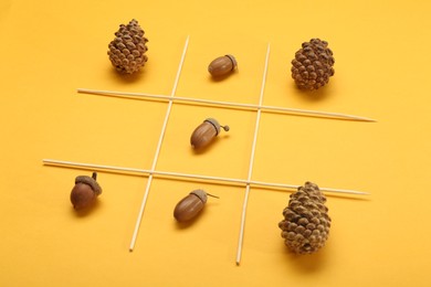 Tic tac toe game made with acorns and pine cones on yellow background