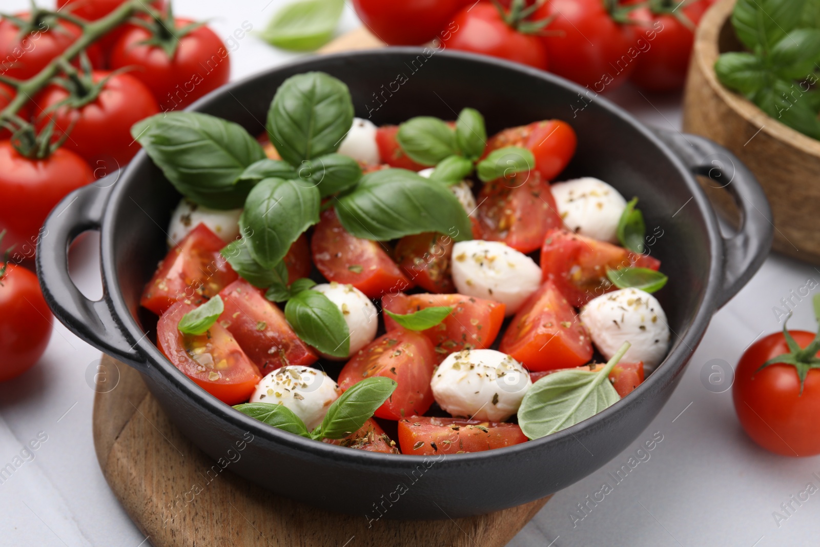 Photo of Tasty salad Caprese with mozarella balls, tomatoes and basil on white table, closeup