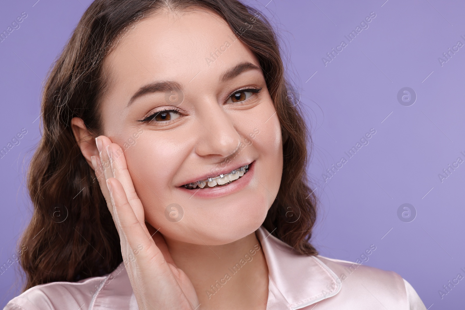 Photo of Smiling woman with dental braces on violet background. Space for text
