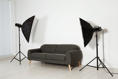 Photo of Comfortable sofa and professional lighting equipment in photo studio