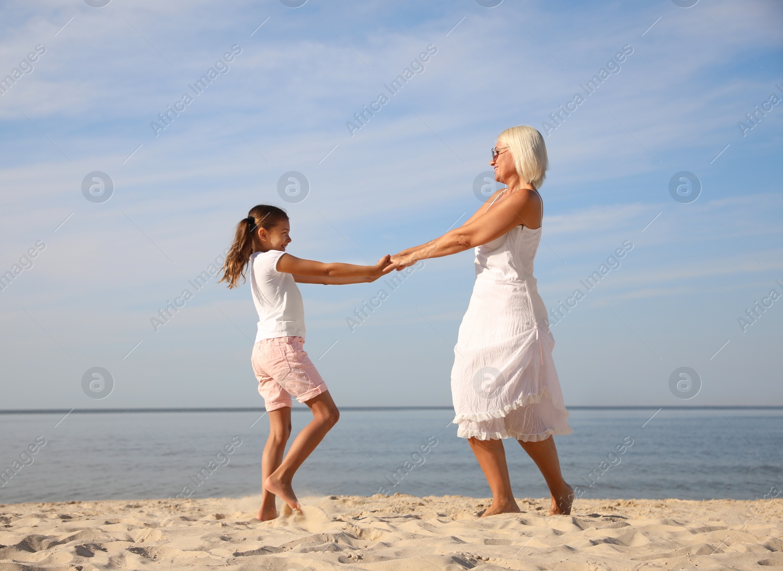 Photo of Cute little girl with grandmother spending time together on sea beach