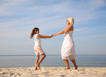 Photo of Cute little girl with grandmother spending time together on sea beach