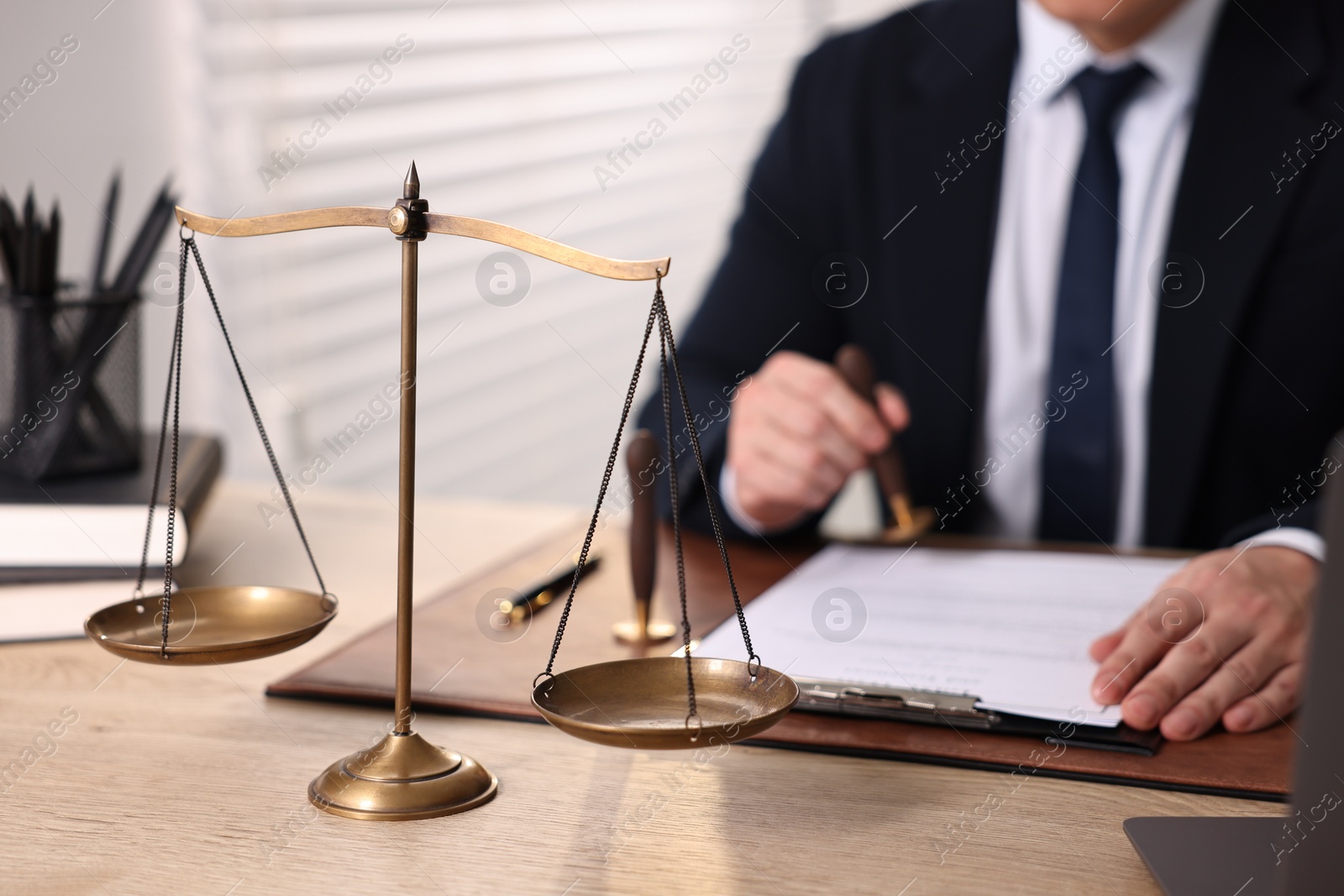 Photo of Notary stamping document at wooden table in office, focus on scales of justice