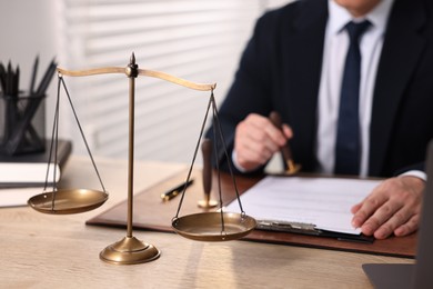 Notary stamping document at wooden table in office, focus on scales of justice