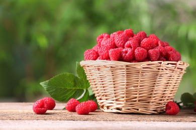 Photo of Wicker basket with tasty ripe raspberries and green leaves on wooden table outdoors. Space for text