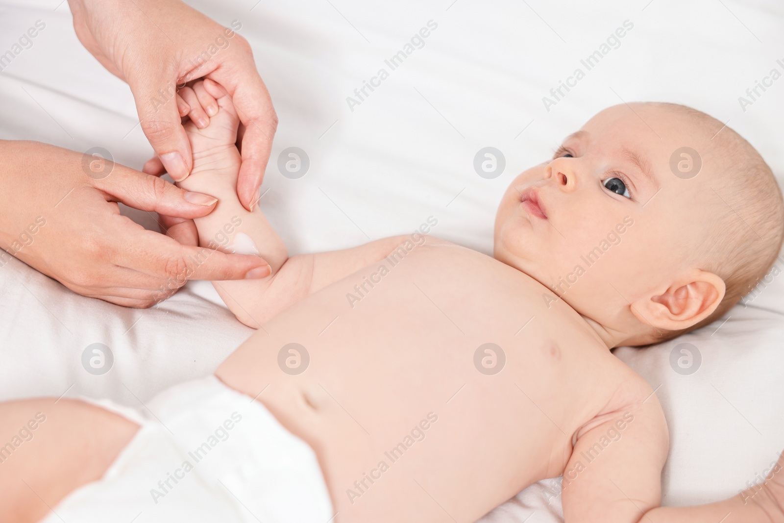 Photo of Woman applying body cream onto baby`s skin on bed, closeup