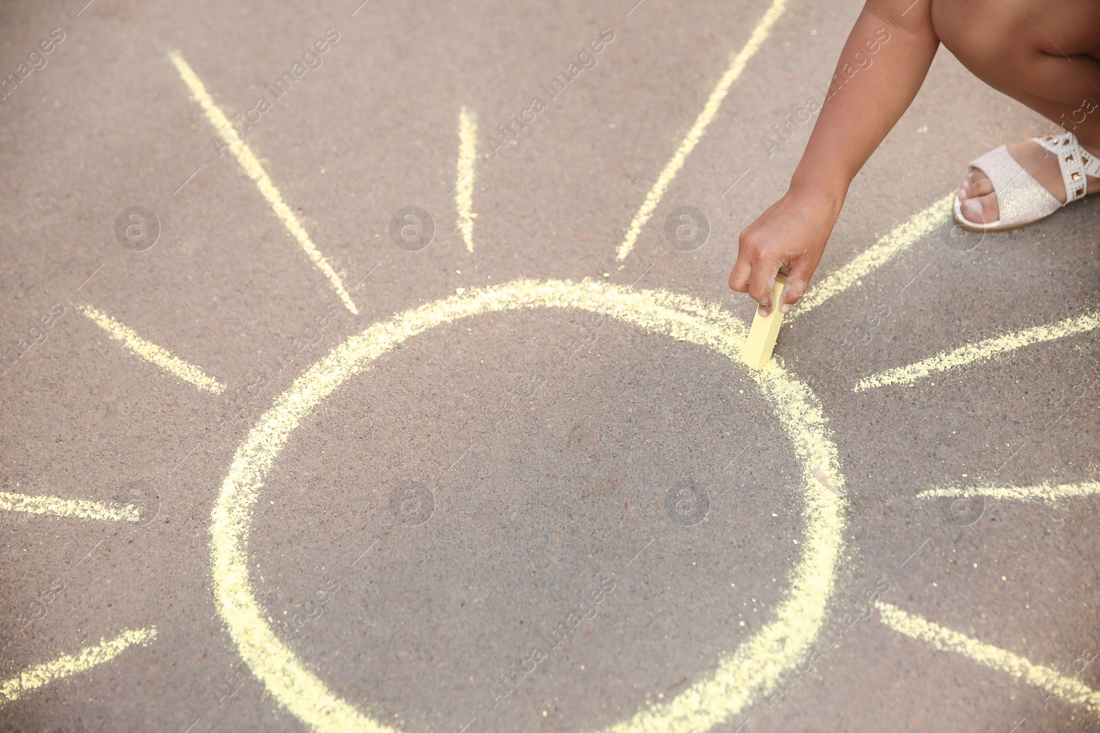 Photo of Little child drawing sun with chalk on asphalt