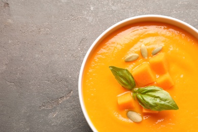 Photo of Bowl with tasty pumpkin soup and space for text on gray background, top view