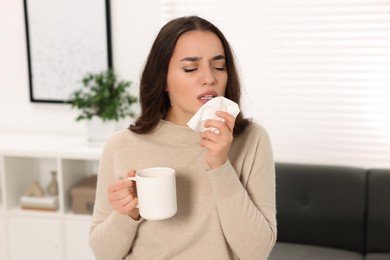 Photo of Sick woman with tissue and cup of drink at home. Cold symptoms