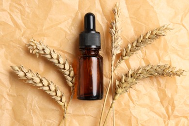 Photo of Bottle with organic cosmetic product and ears of wheat on parchment paper, flat lay