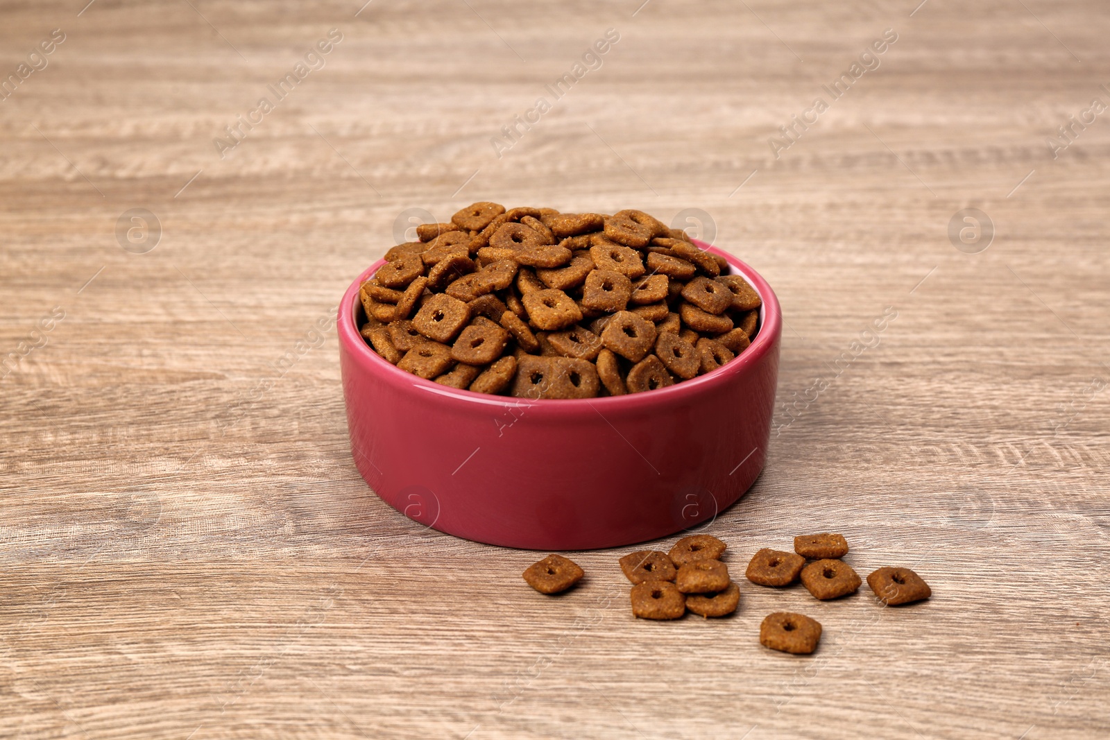 Photo of Dry food in pet bowl on wooden surface