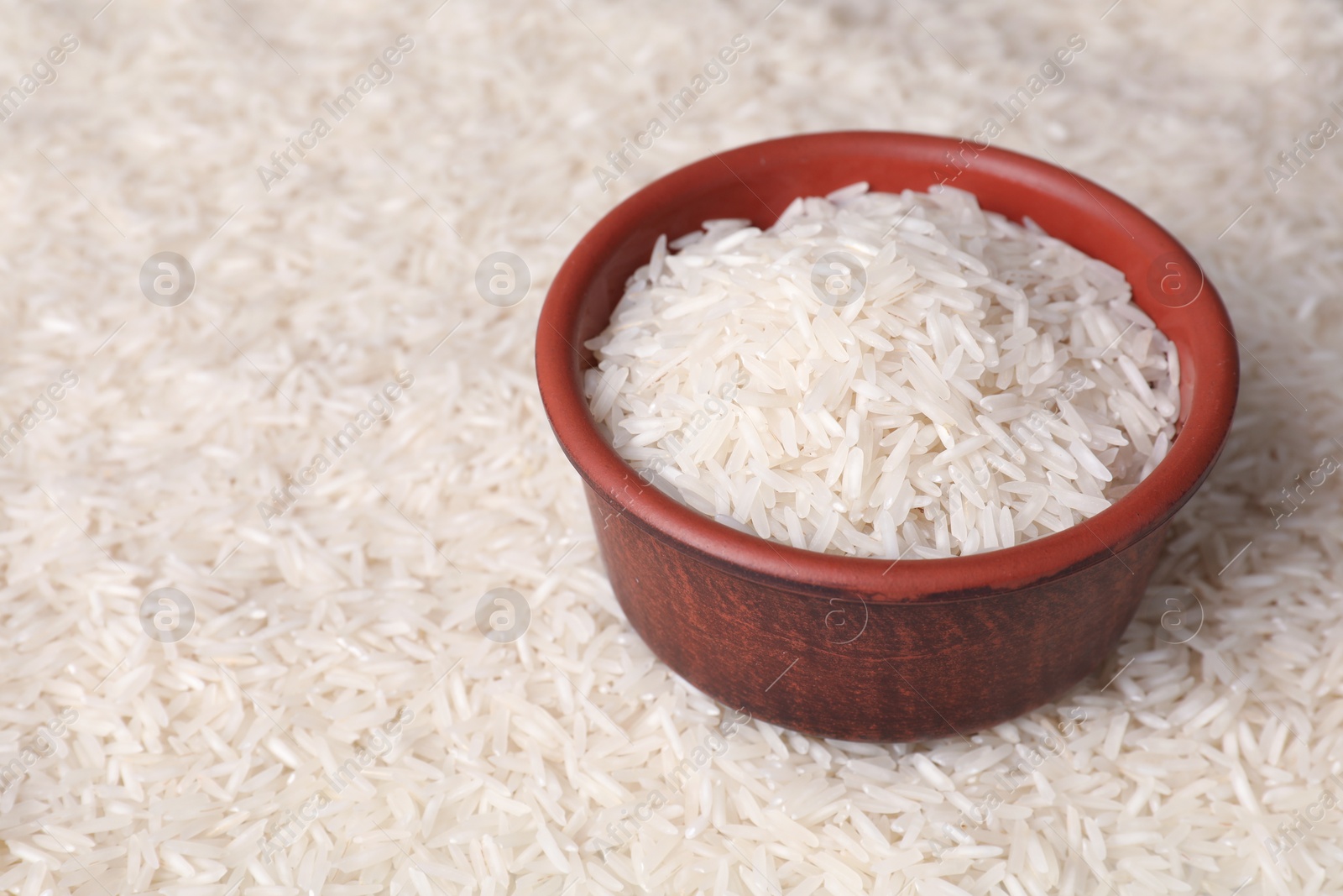 Photo of Raw basmati rice and bowl as background, closeup. Space for text