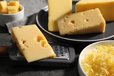 Grated, whole pieces of cheese and grater on dark textured table, closeup