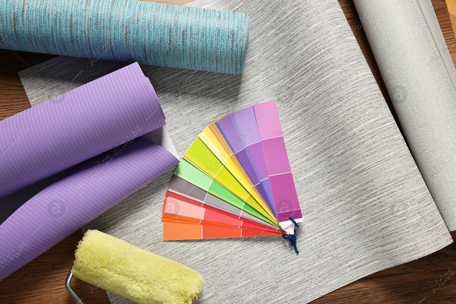 Photo of Different wallpaper rolls, roller and color palette samples on wooden table, flat lay