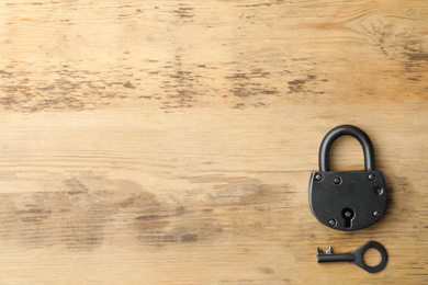 Steel padlock, key and space for text on wooden background, top view. Safety concept