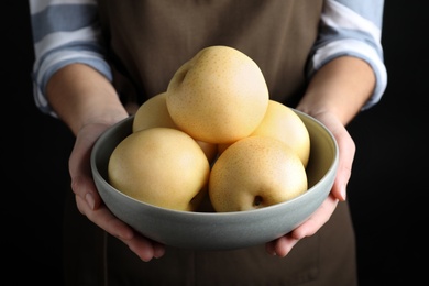 Photo of Woman holding bowl with ripe apple pears on black background, closeup
