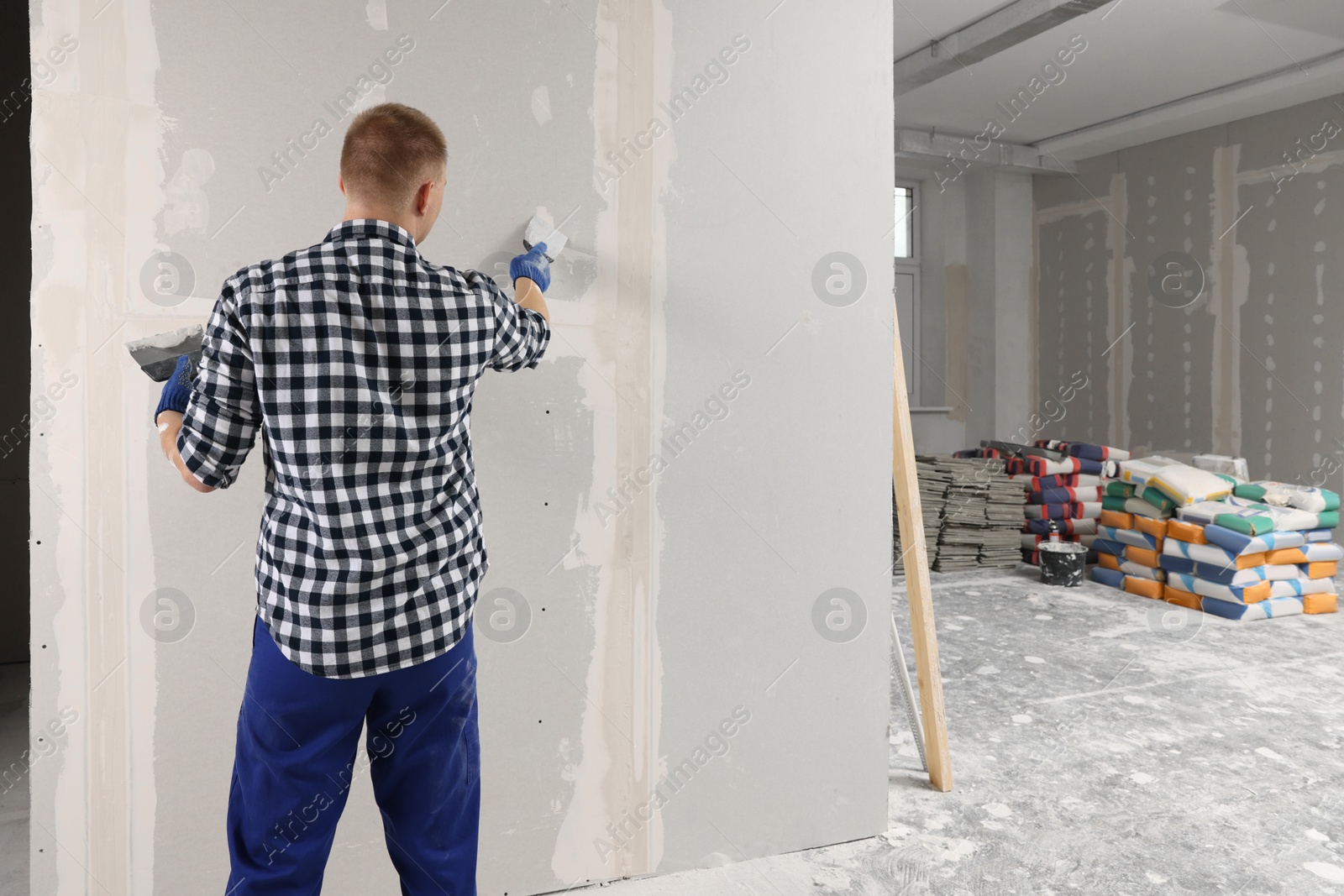 Photo of Man plastering wall with putty knife indoors, back view and space for text. Home renovation