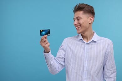 Photo of Happy man with credit card on light blue background. Space for text