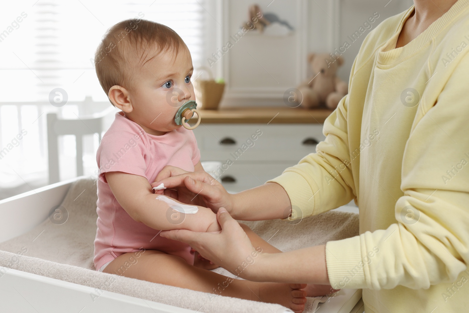 Photo of Mother applying body cream on her little baby at home, closeup