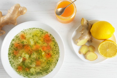 Flat lay composition with bowl of fresh homemade soup to cure flu on wooden background