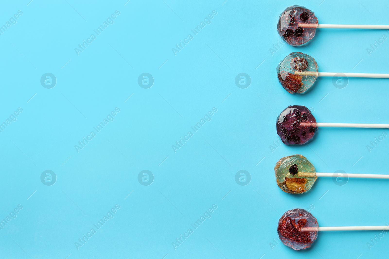 Photo of Sweet colorful lollipops with berries on light blue background, flat lay. Space for text