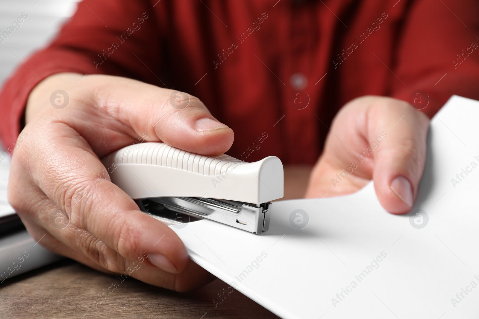 Photo of Man stapling papers at wooden table, closeup