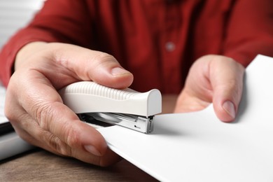 Photo of Man stapling papers at wooden table, closeup