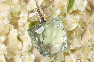 Bottle of aromatic perfume among jasmine flowers on beige background, flat lay