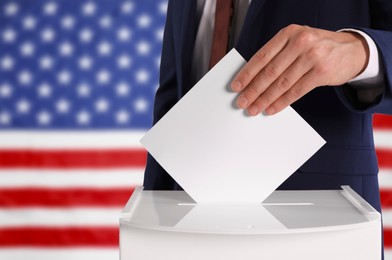 Election in USA. Man putting his vote into ballot box against national flag of United States, closeup