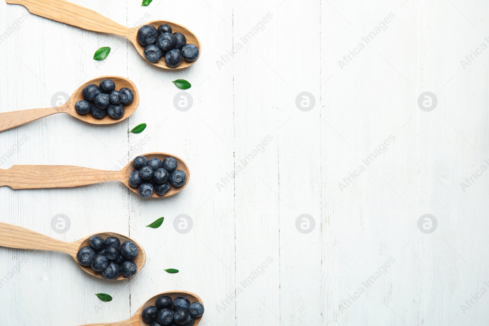 Photo of Flat lay composition of spoons with tasty blueberries and leaves on white wooden table, space for text