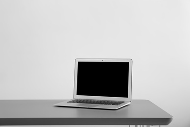 Photo of Modern laptop with blank screen on table against light background
