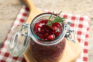 Photo of Fresh cranberry sauce in glass jar and rosemary on table, closeup