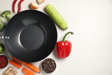 Empty iron wok surrounded by raw ingredients on white wooden table, flat lay. Space for text