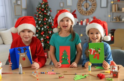 Photo of Cute little children in Santa hats making beautiful Christmas greeting cards at home
