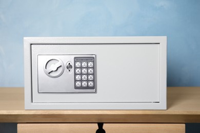 Photo of Closed steel safe on wooden table against light blue background