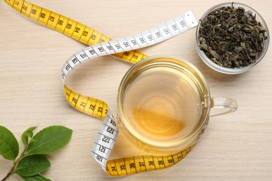 Photo of Composition with glass cup of diet herbal tea and measuring tape on wooden background, flat lay