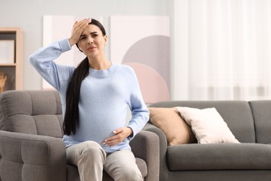 Photo of Pregnant woman suffering from headache on armchair at home