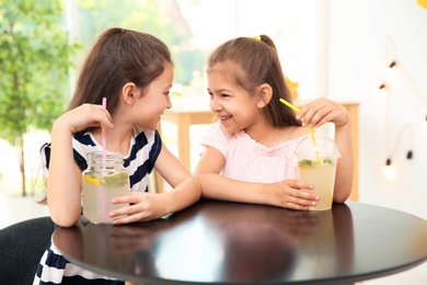 Photo of Little girls with natural lemonade at table indoors