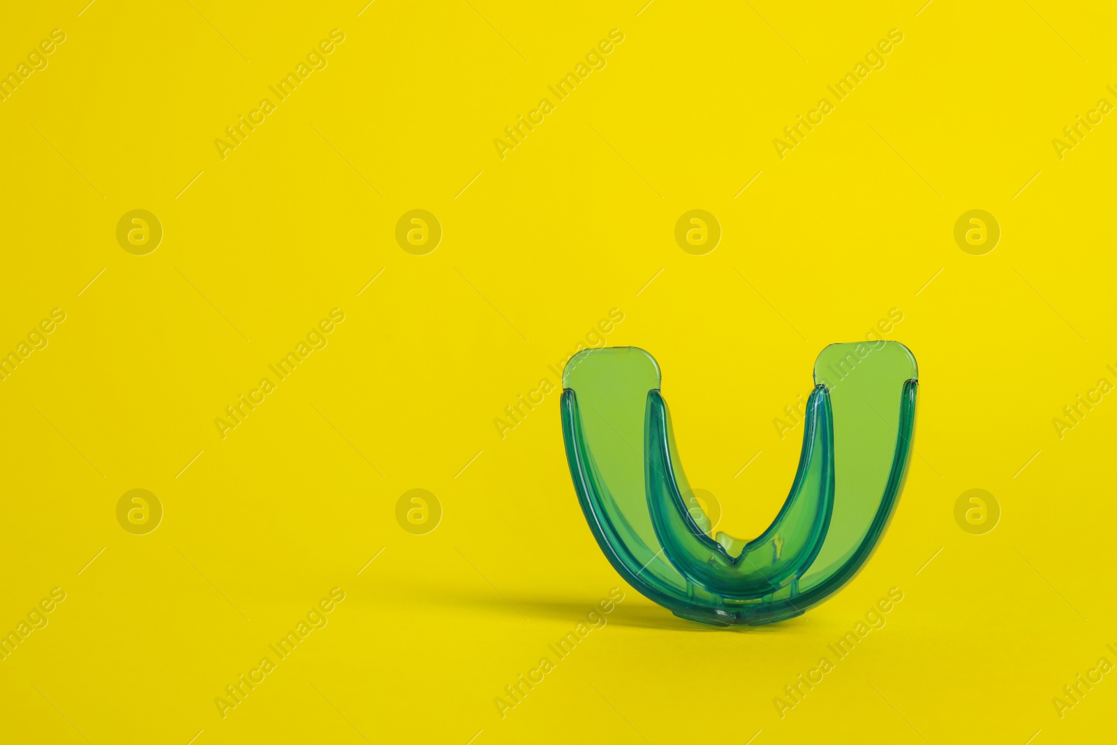 Photo of Transparent dental mouth guard on yellow background, space for text. Bite correction