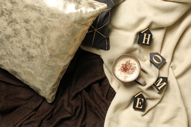 Photo of Flat lay composition with word HOME, cup of coffee, pillows and warm plaid on bed